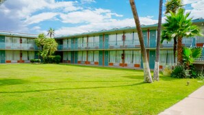 A motel with a green lawn, palm trees, and a two-story building with balconies. - GLH Hotel (Tucson)