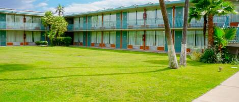 A motel with a green lawn, palm trees, and a two-story building with balconies.
