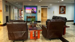A lobby with leather sofas, a coffee table, a TV displaying 'Titanic', and a 'Palo Verde' sign. - GLH Hotel (Tucson)