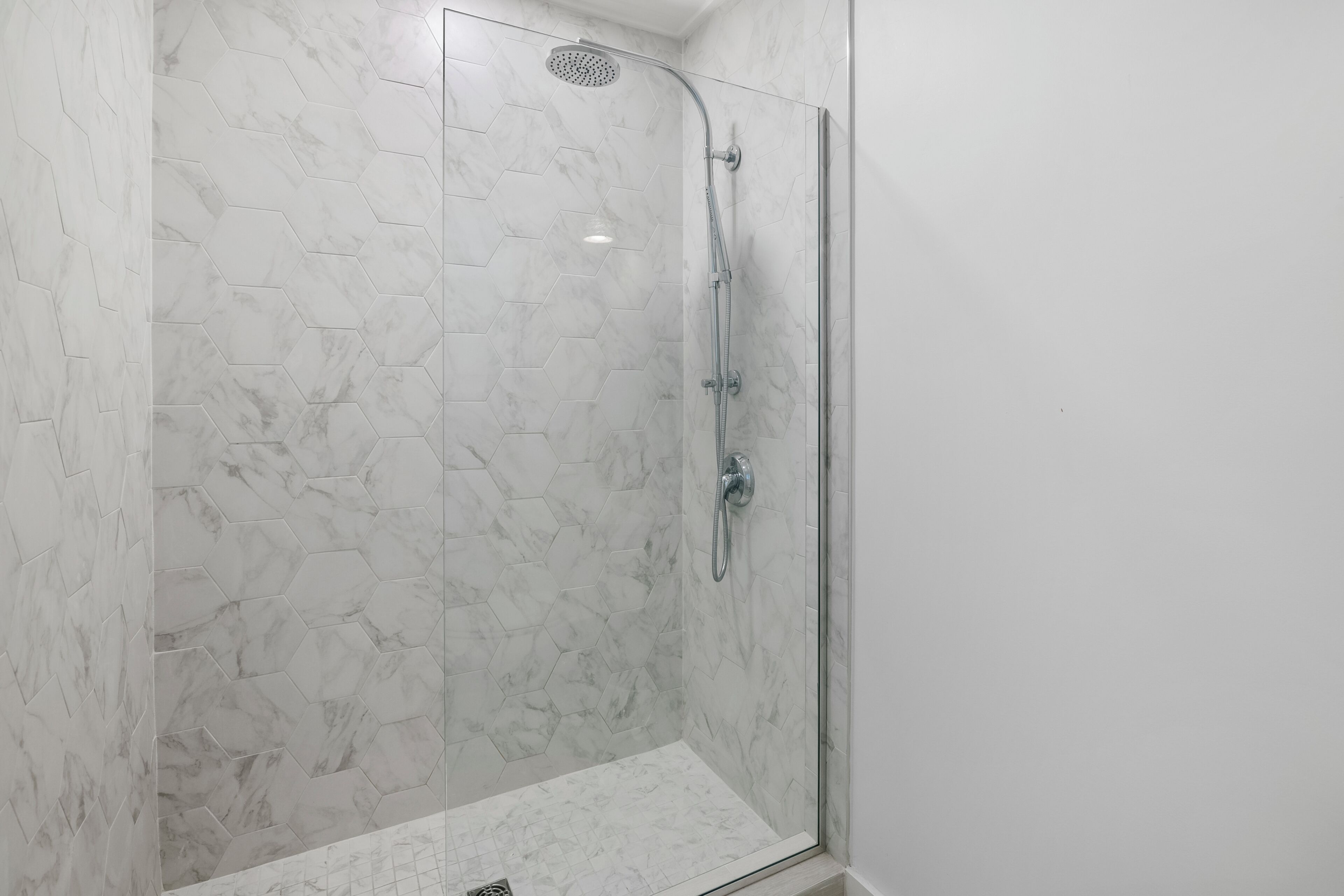 Ducha con paredes y suelo de baldosas hexagonales, protegida por un cerramiento de cristal.