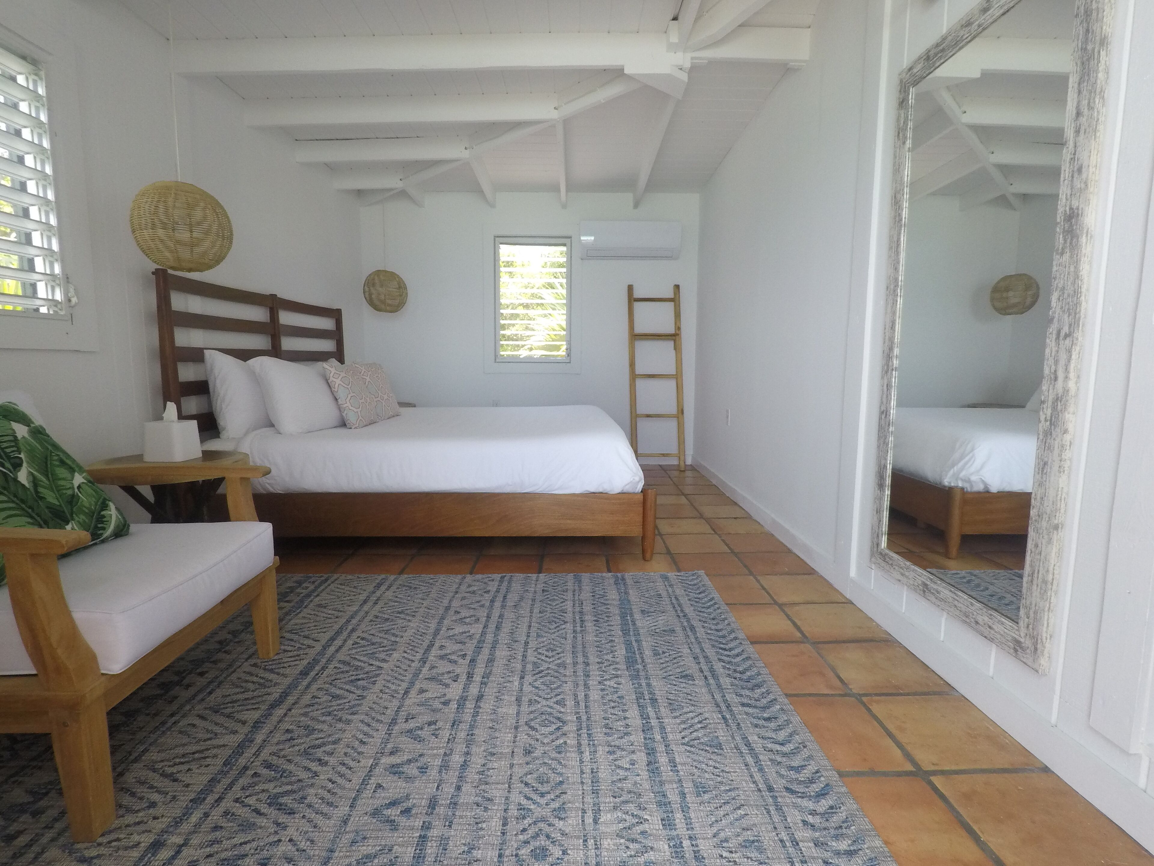 A bedroom with a wooden bed, a small bedside table, a chair, a patterned rug, a ladder, and a large mirror.