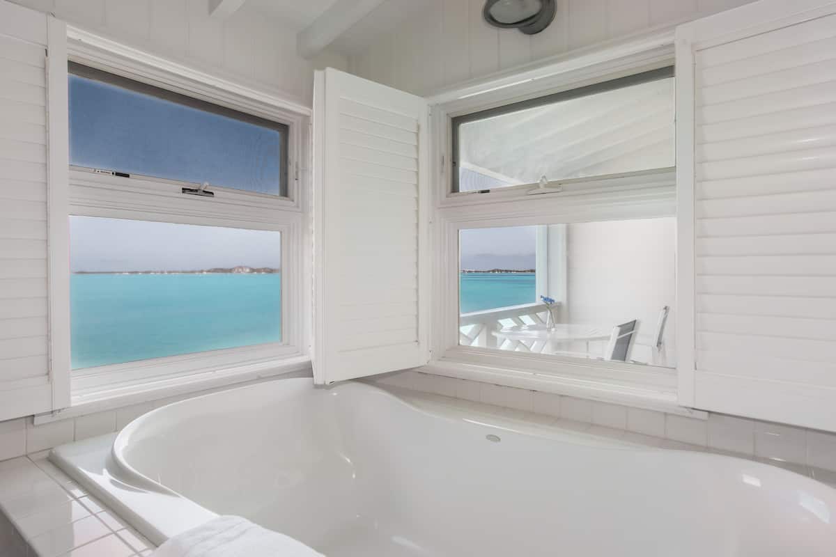 A bathroom with a bathtub, large windows, and a view of the sea.