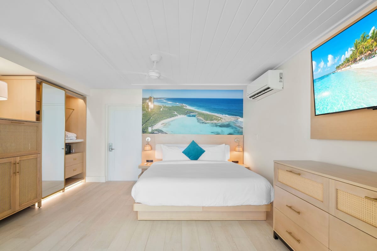 A bedroom with a large bed, a wardrobe, a TV, and a beach view mural.