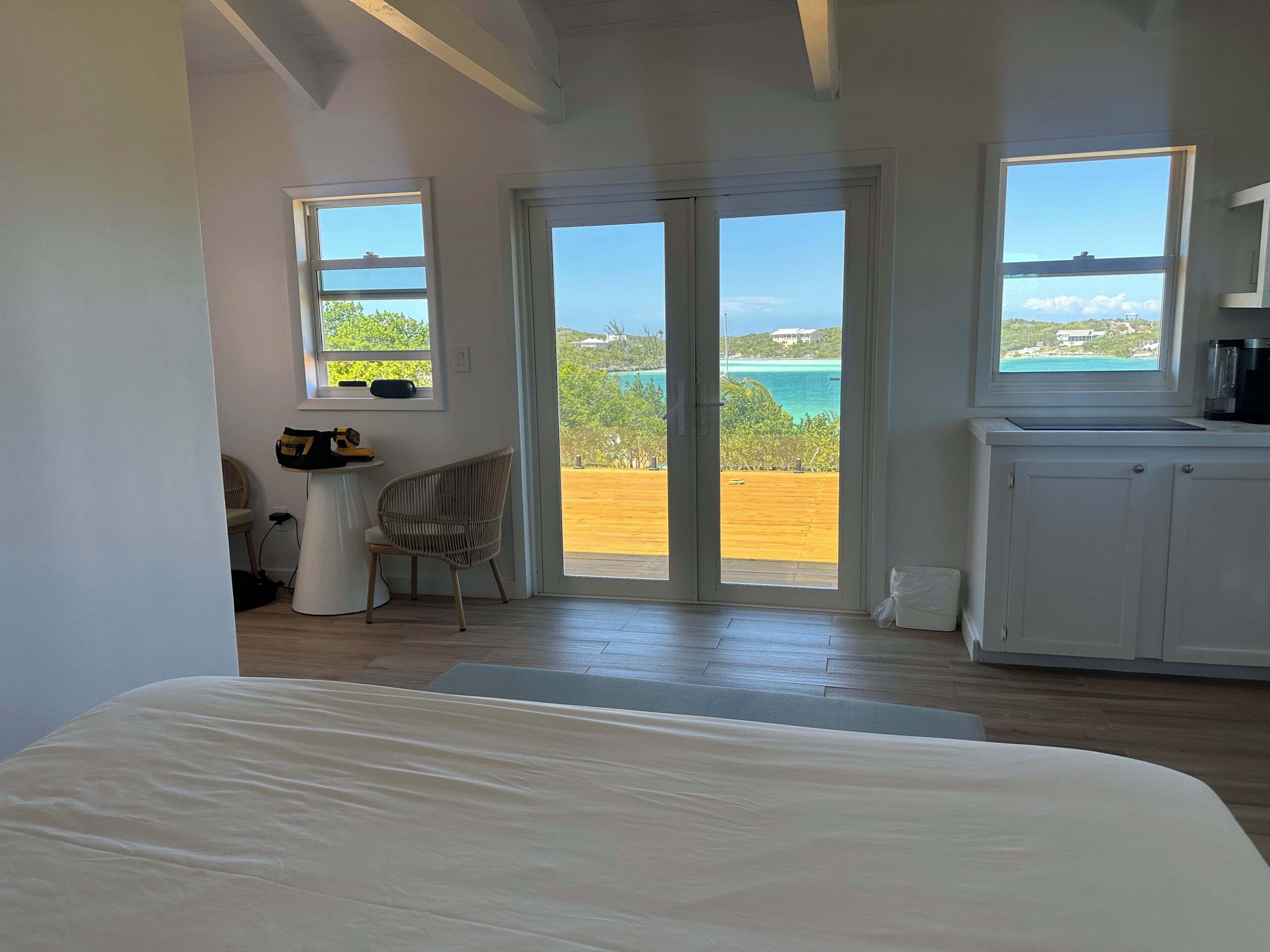 A bedroom with a large bed, a chair, a desk, and a view of the sea through a sliding door.