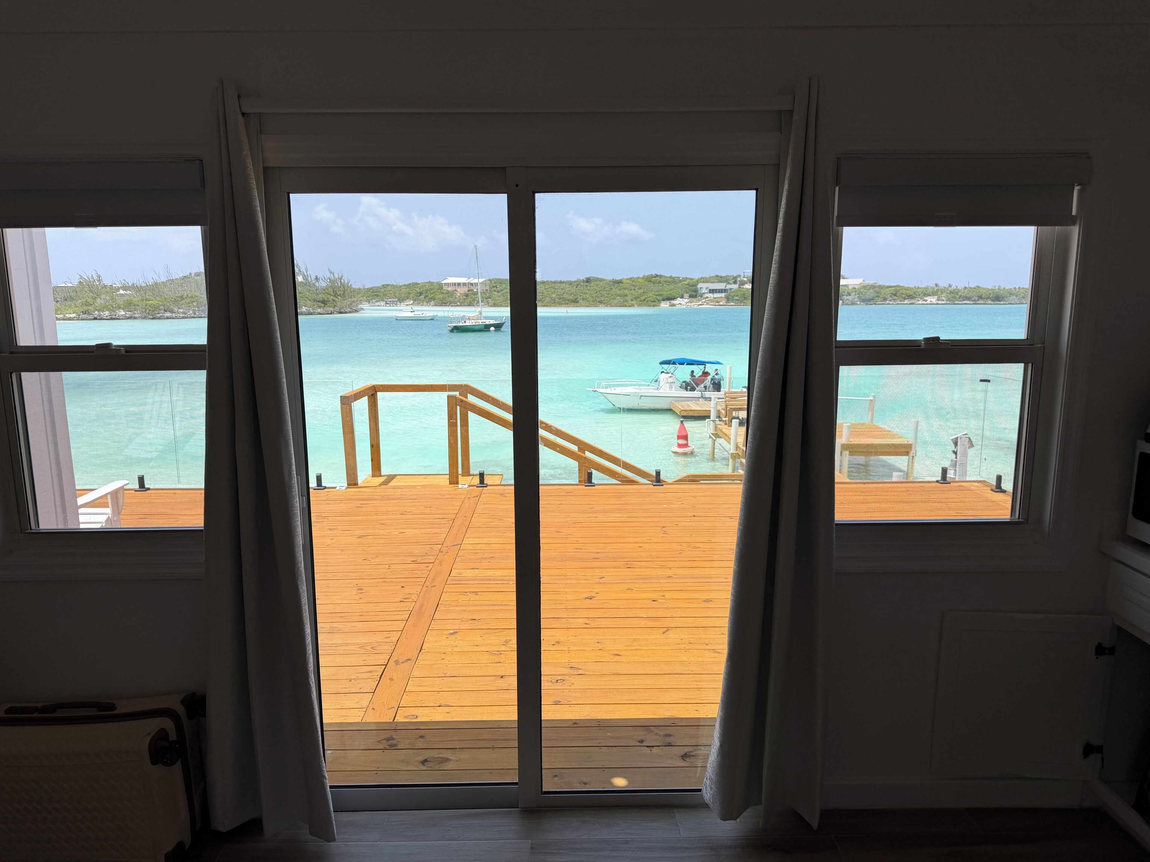 Une chambre avec vue sur une terrasse en bois qui mène à un quai où sont amarrés des bateaux.