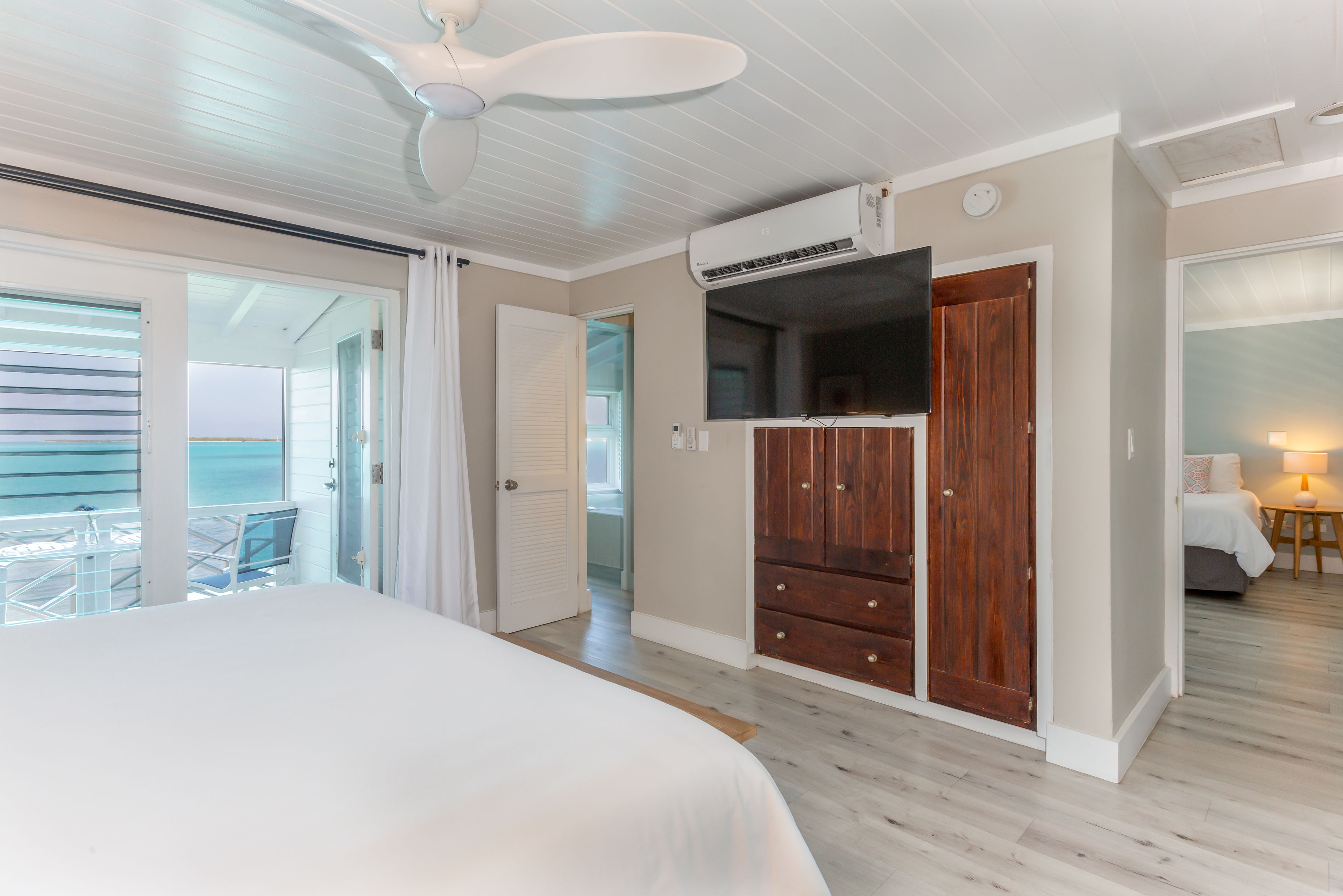 Ein Schlafzimmer mit einem Bett, einem Deckenventilator, einer Klimaanlage, einem Holzschrank und Blick auf den Balkon.