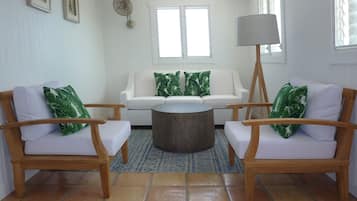 Un salon avec deux fauteuils en bois, un canapé blanc, une table basse ronde et un lampadaire.