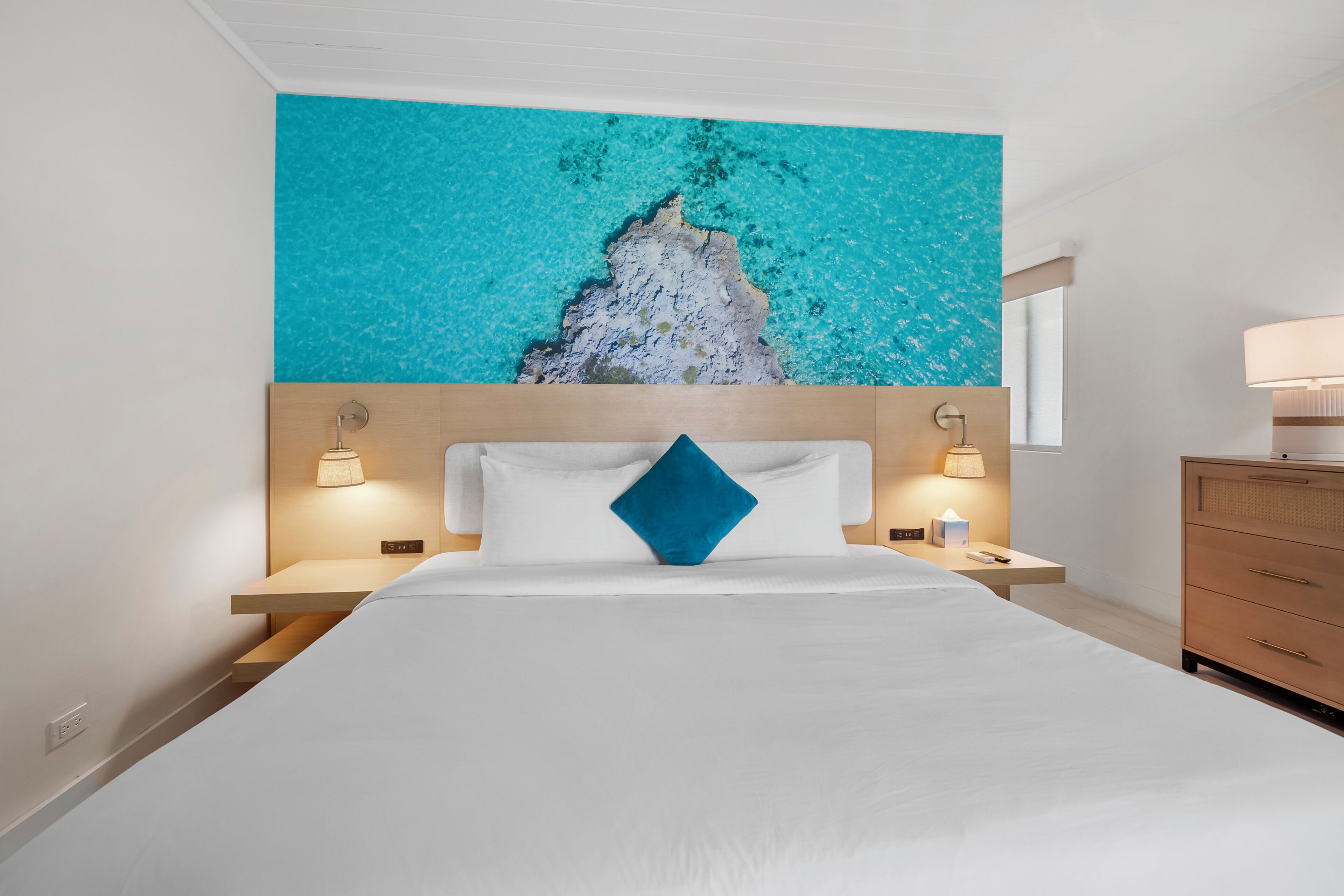 Una habitación de hotel con una cama grande, una mesita de noche con lámpara, un aparador y una obra de arte en la pared.