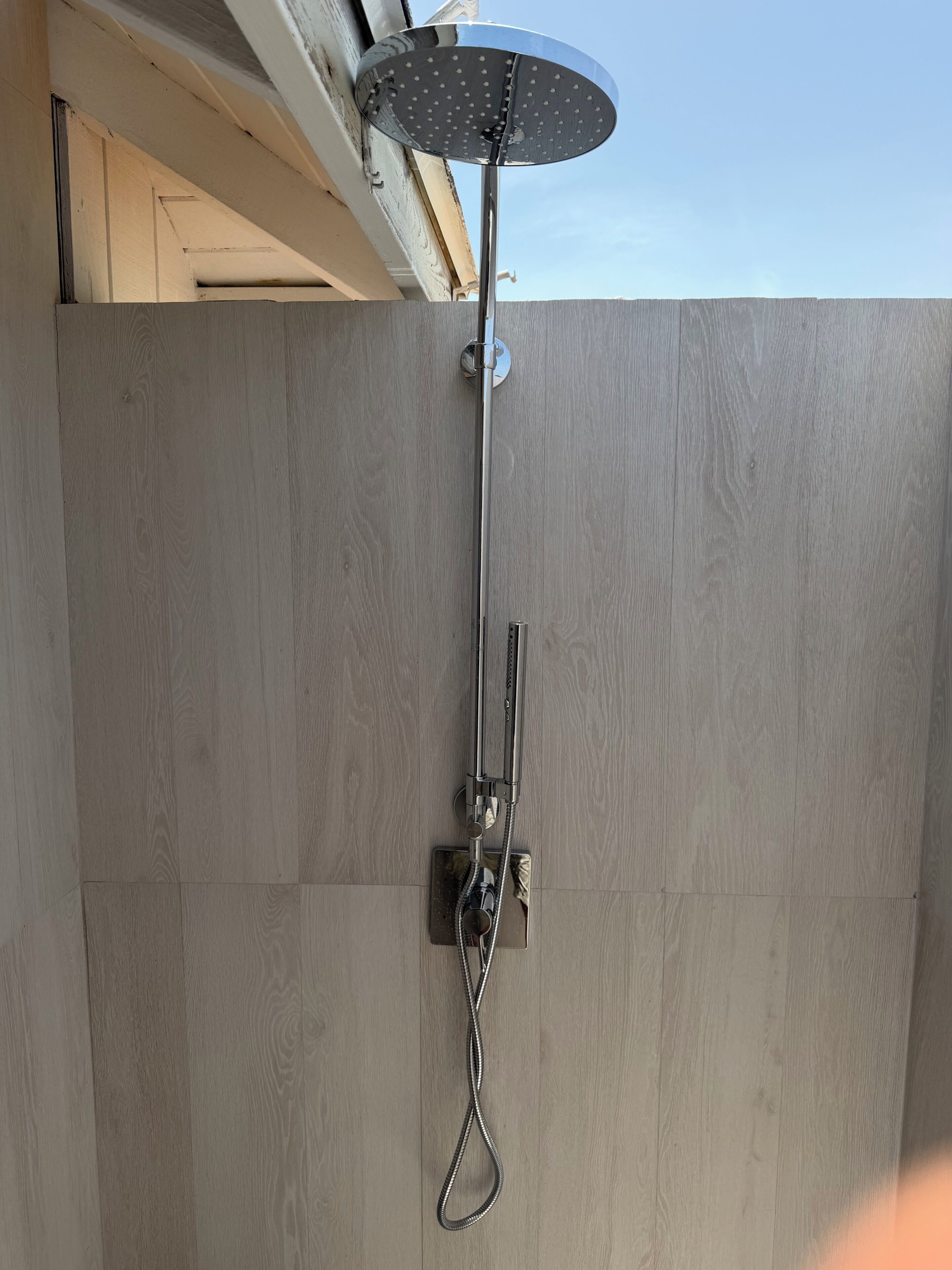 A showerhead with a rain shower attachment, mounted on a wall with a wooden panel design.