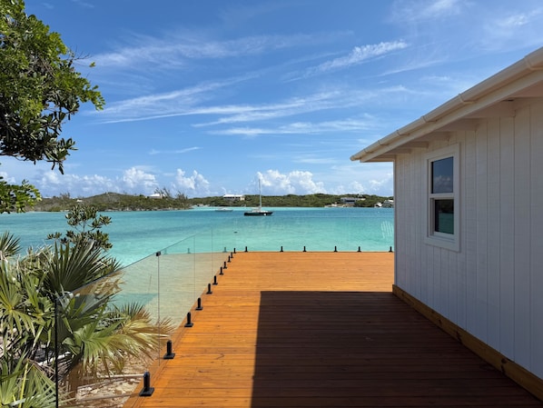 A wooden deck leading to a white building with a view of a turquoise sea and boats.