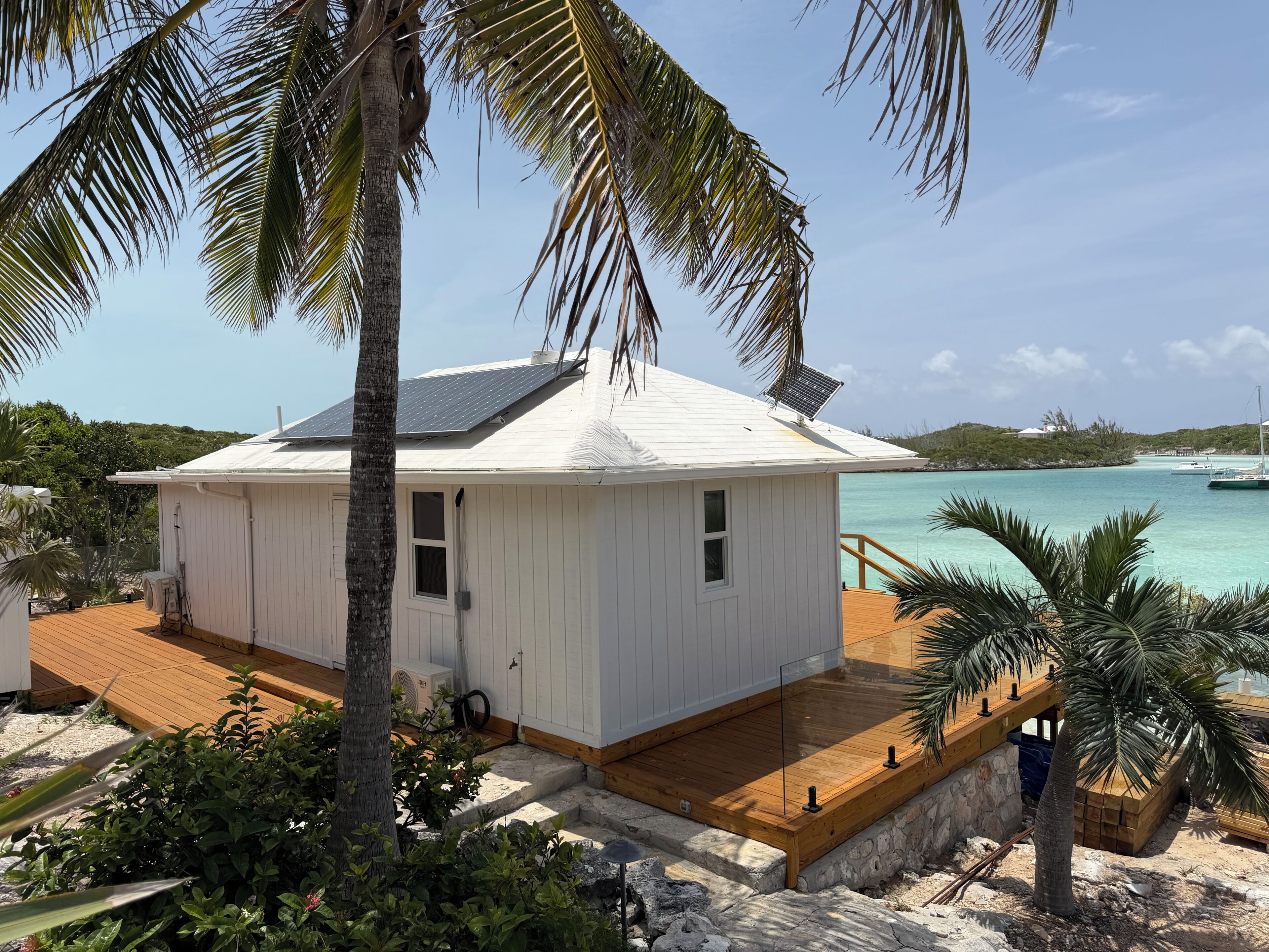 A white building with a wooden deck, surrounded by tropical vegetation and overlooking a turquoise sea.