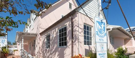 A pink building with a sign for the Exuma Peace Inn Hotel, offering breakfast, lunch, and dinner.