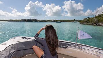 A person on a boat with a flag labeled "Peace & Plenty" and a view of a calm sea and distant shoreline.
