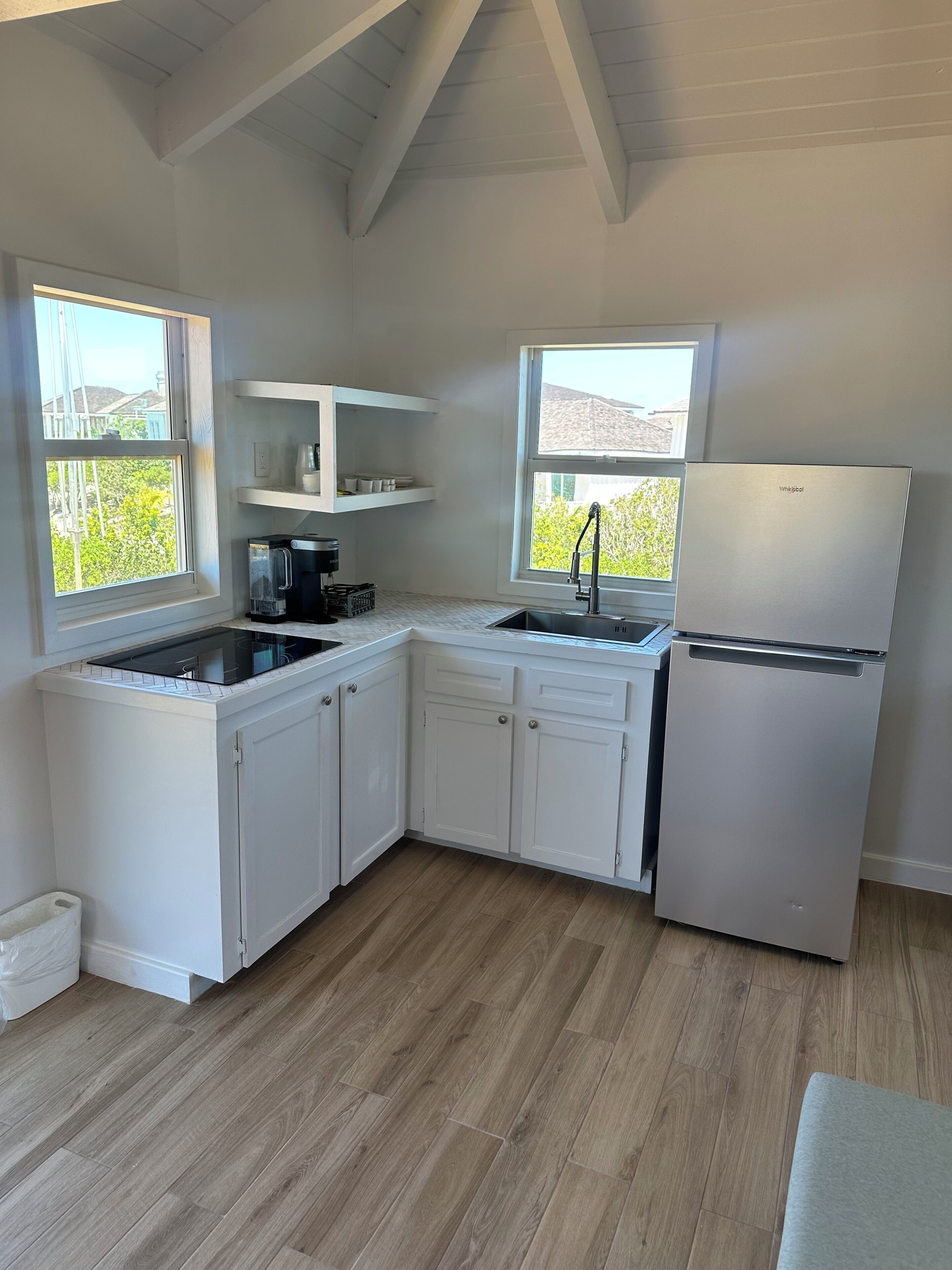 Cocina con armarios blancos, encimera negra, refrigerador y dos ventanas.