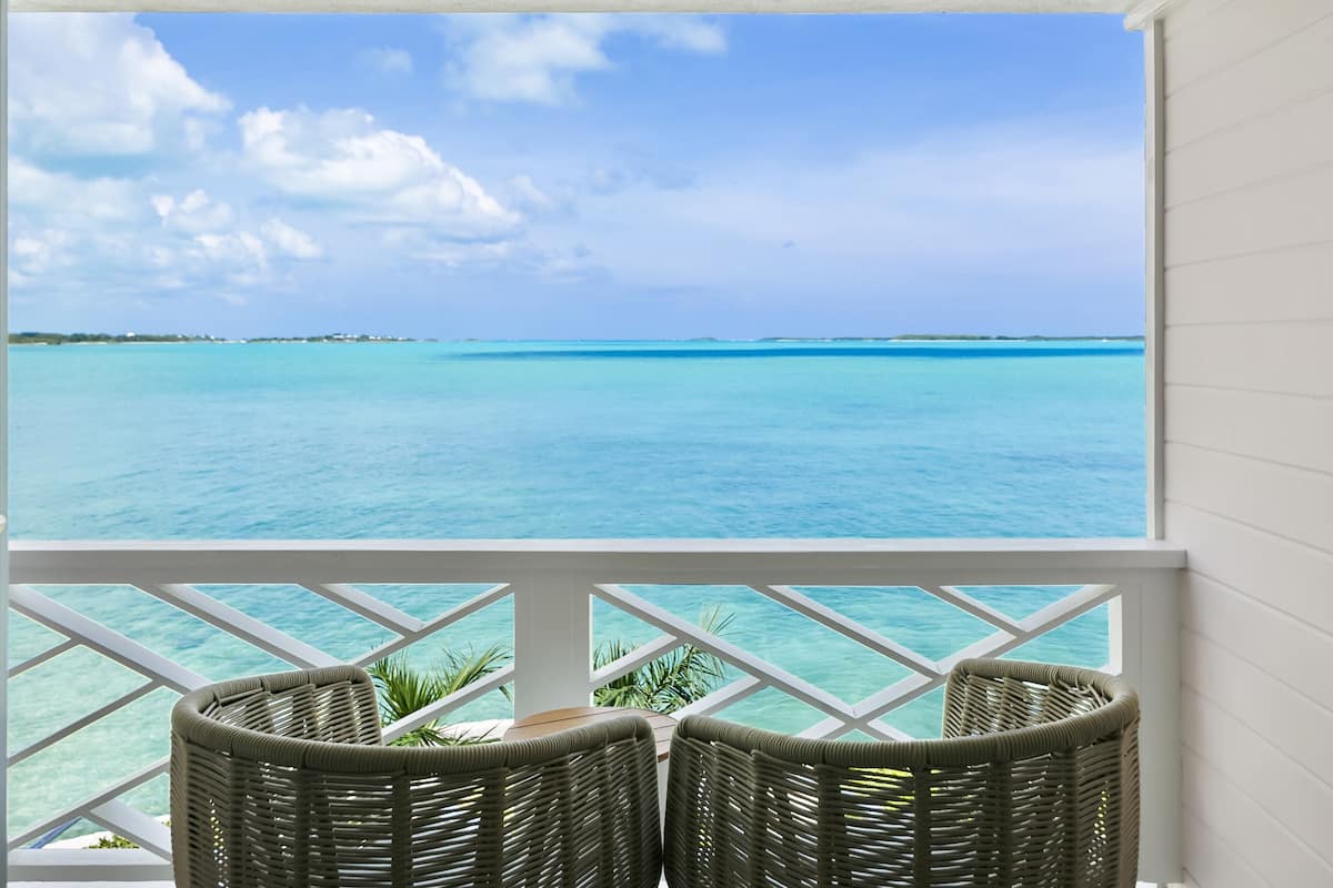 A balcony with wicker chairs overlooking turquoise waters and a clear sky.