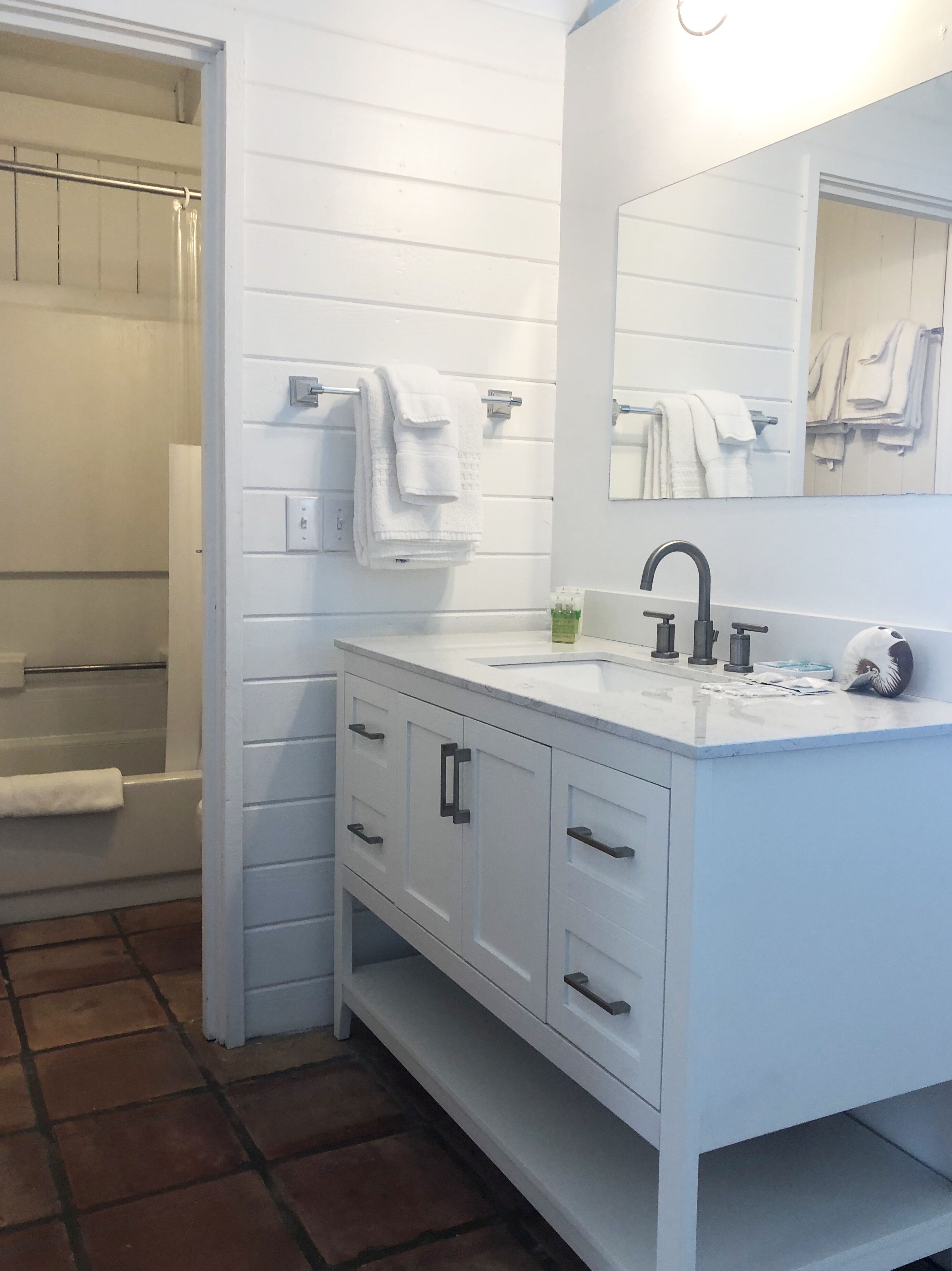 Un baño con tocador blanco, lavamanos, espejo y zona de ducha.