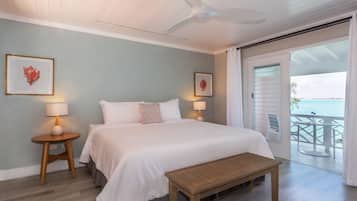 A bedroom with a bed, bedside tables, a bench, ceiling fan, and a balcony with a view.