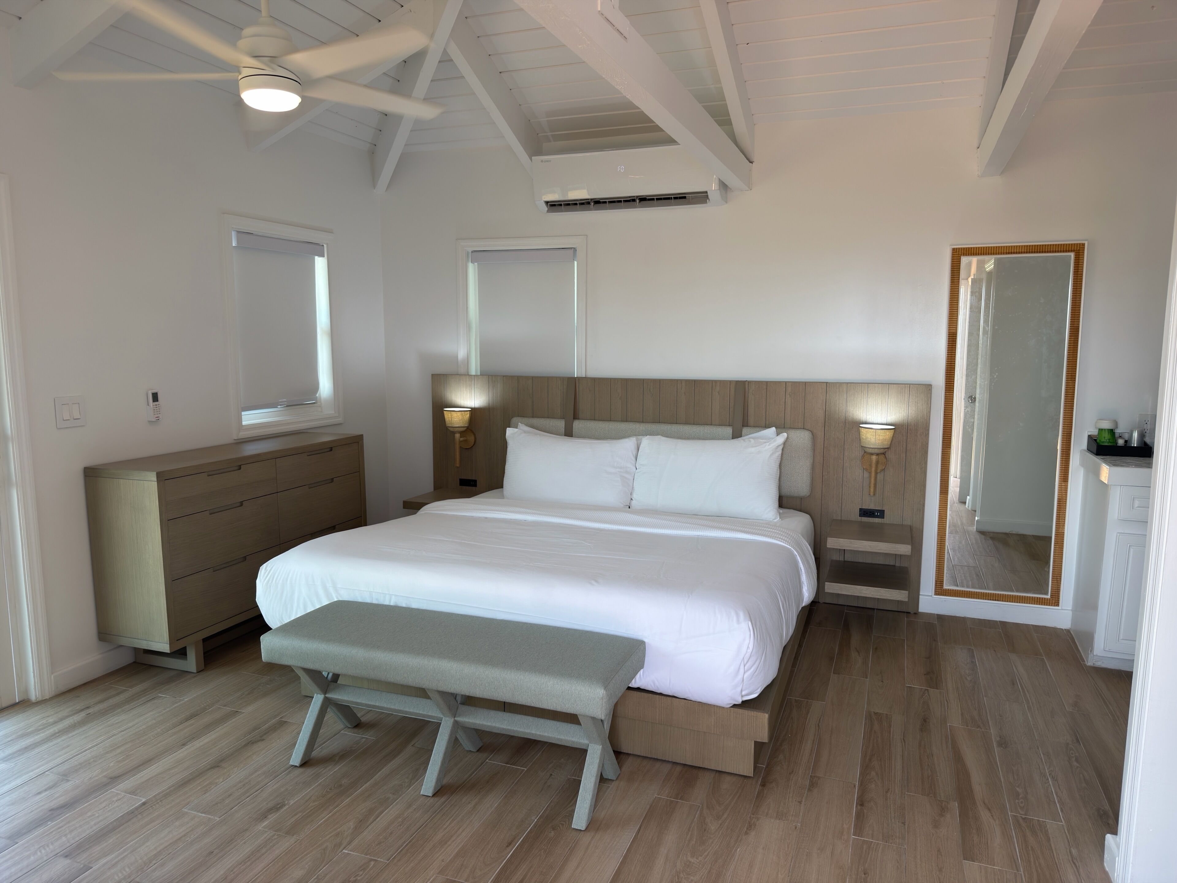 A bedroom with a bed, bench, dresser, bedside lamps, and a ceiling fan.