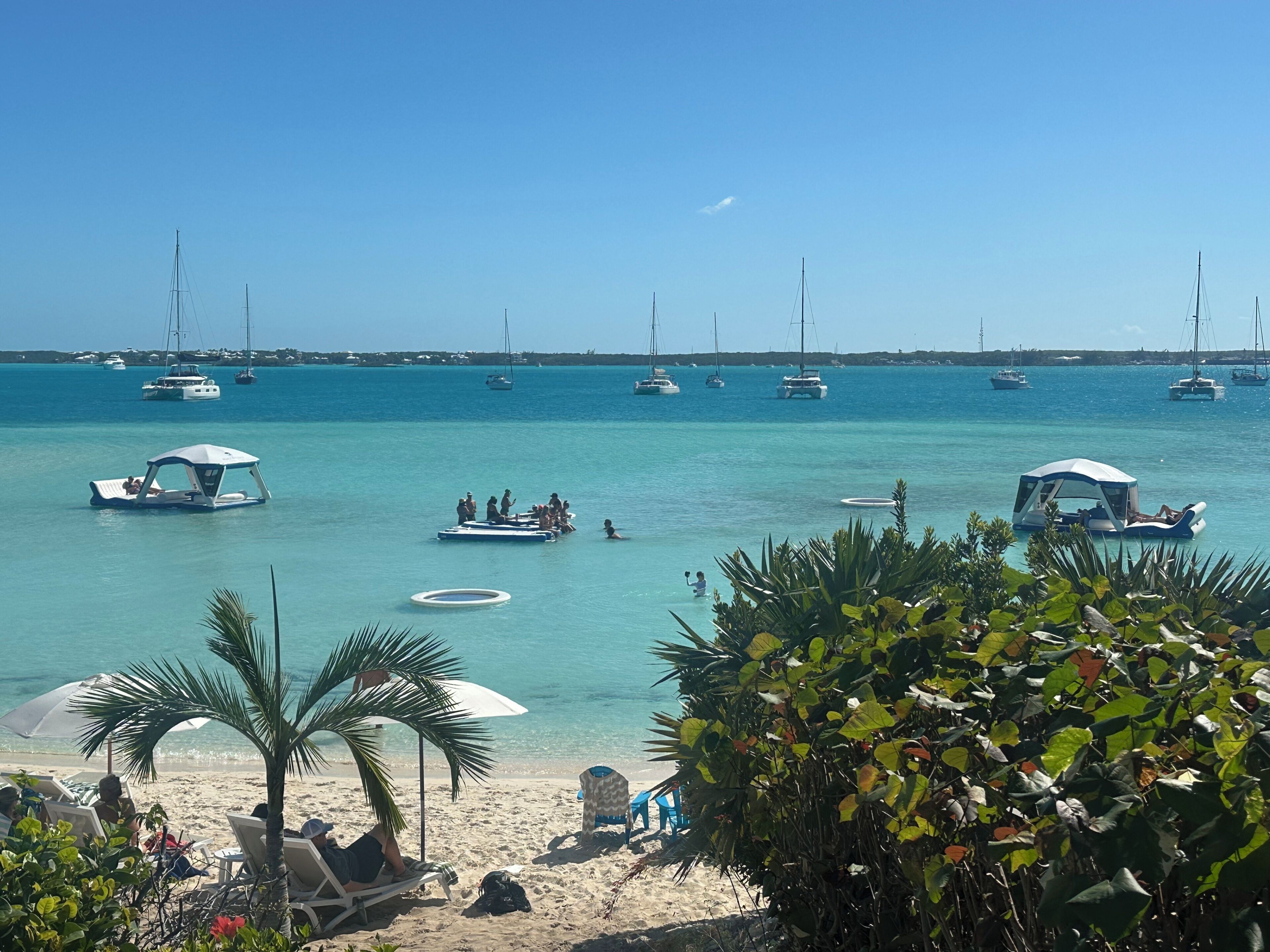 A beach with clear turquoise water, several boats, and people enjoying the area.