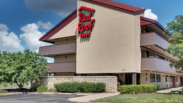 Un hotel Red Roof Inn con una estructura de dos pisos, fachada de piedra y un cielo azul despejado al fondo.