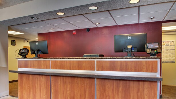 A reception desk with two computer monitors, a cash register, and a wall-mounted calendar. - Red Roof Inn St Louis - Westport/ Maryland Heights (Maryland Heights)