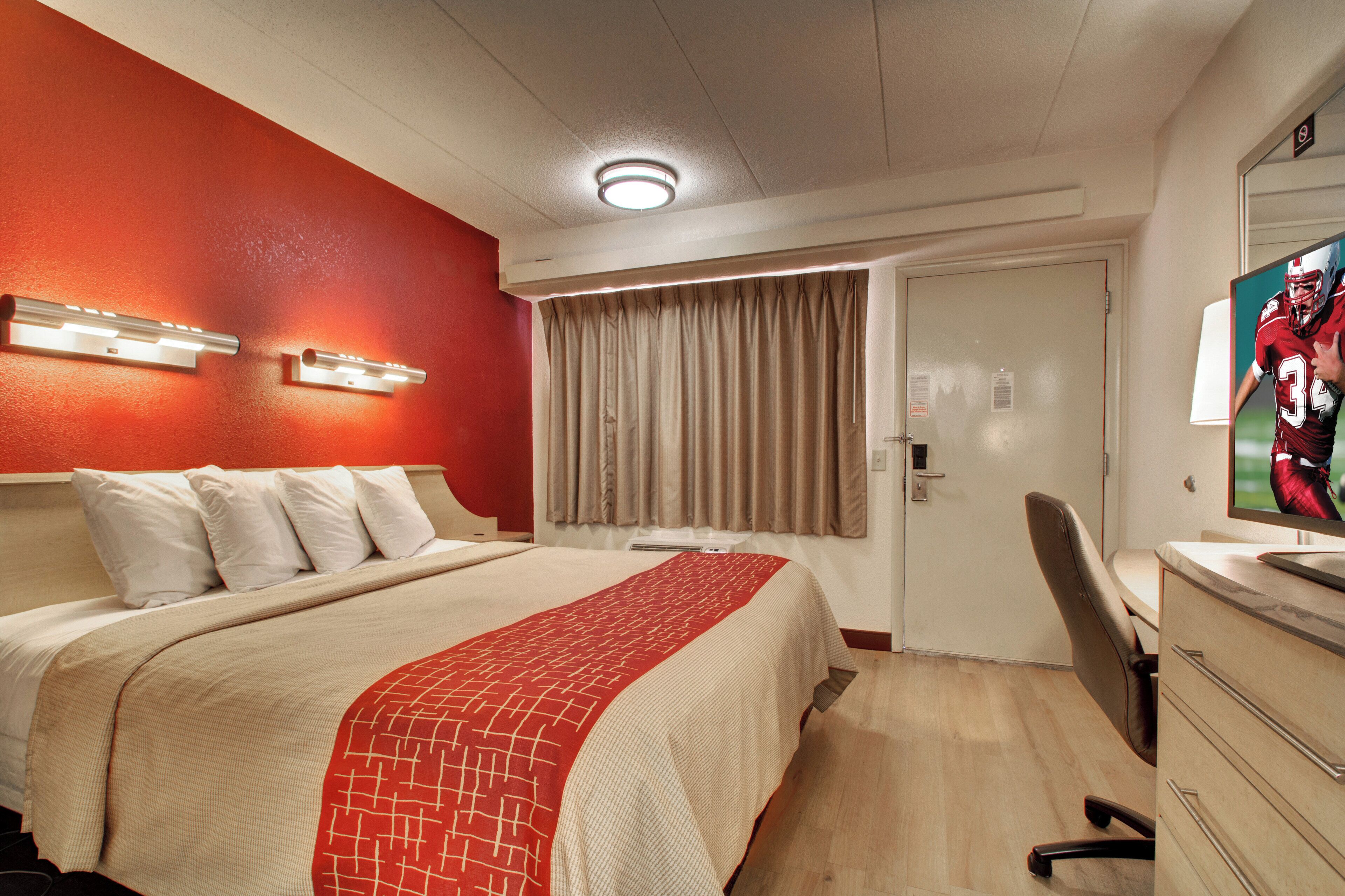 A hotel room with a bed, a desk, a television, and a door.
