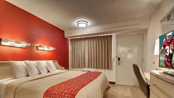 A hotel room with a bed, a desk, a television, and a door.