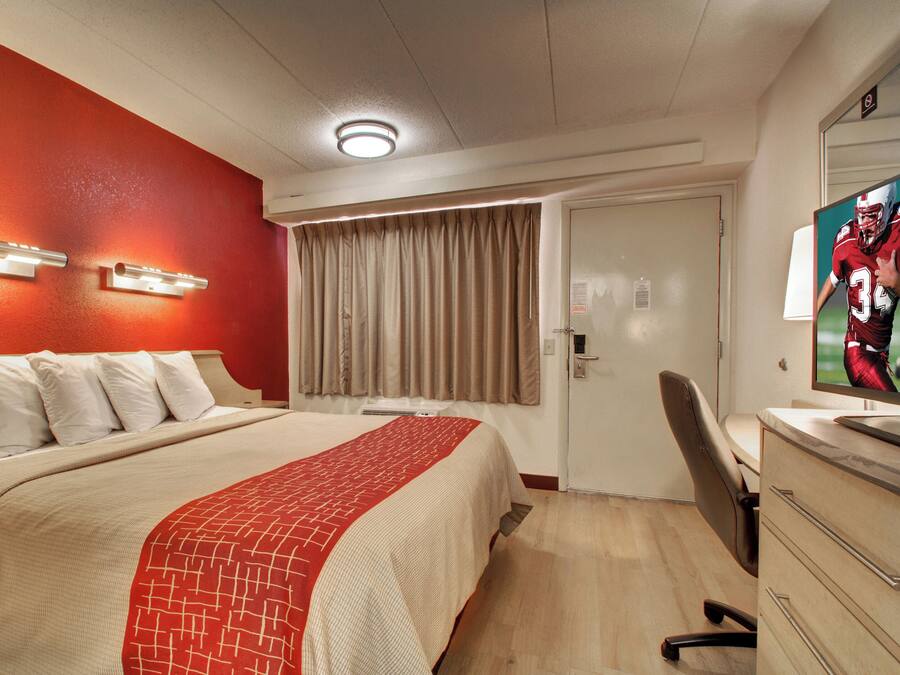 A hotel room with a bed, a desk, a television, and a door.