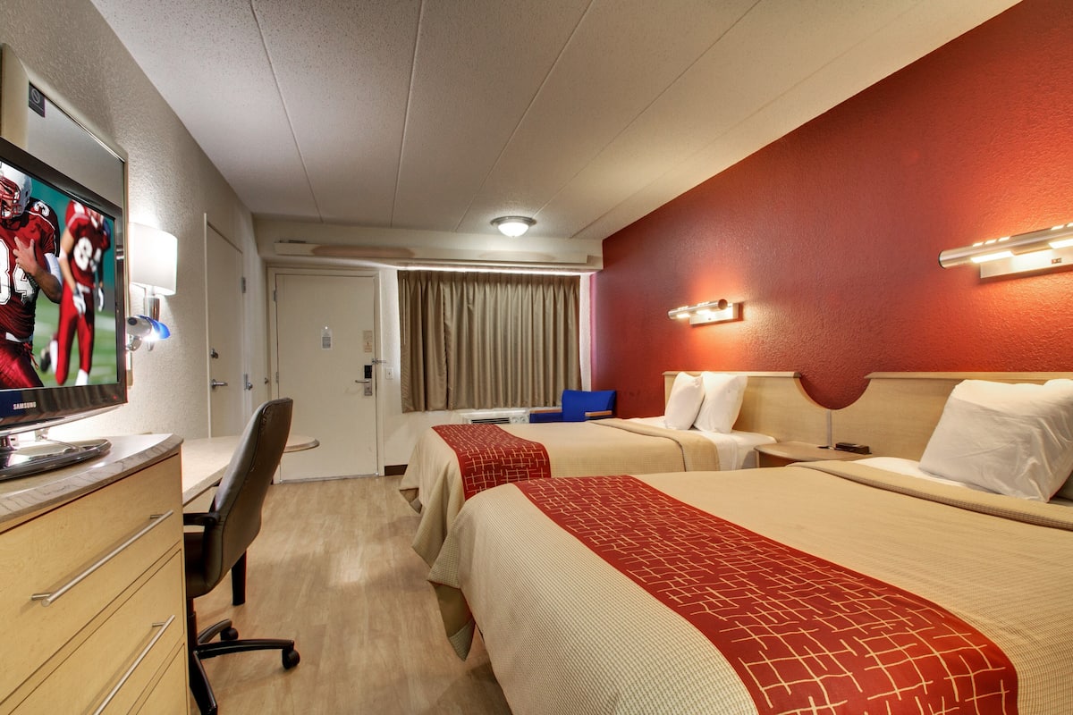 A hotel room with two beds, a desk with a computer, a TV, and a mirror.