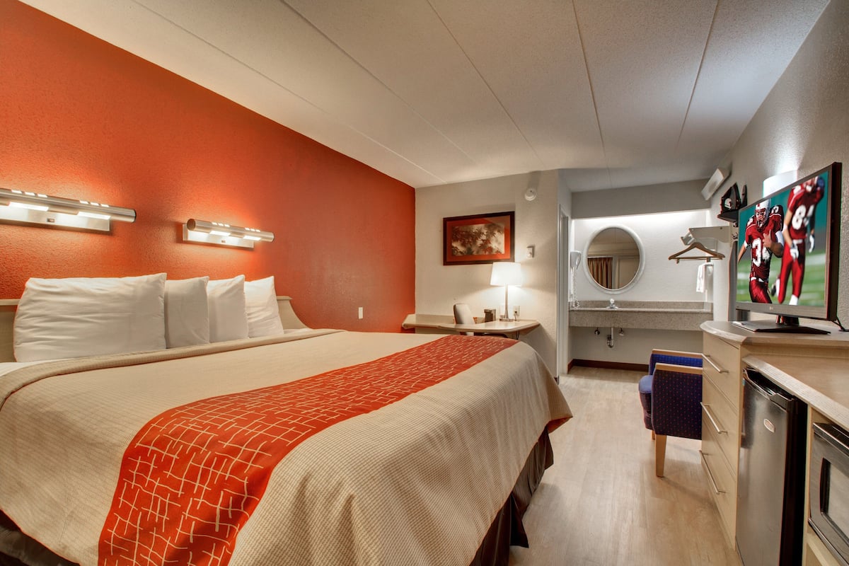 A hotel room with a large bed, a desk, a chair, a TV, and a mirror.