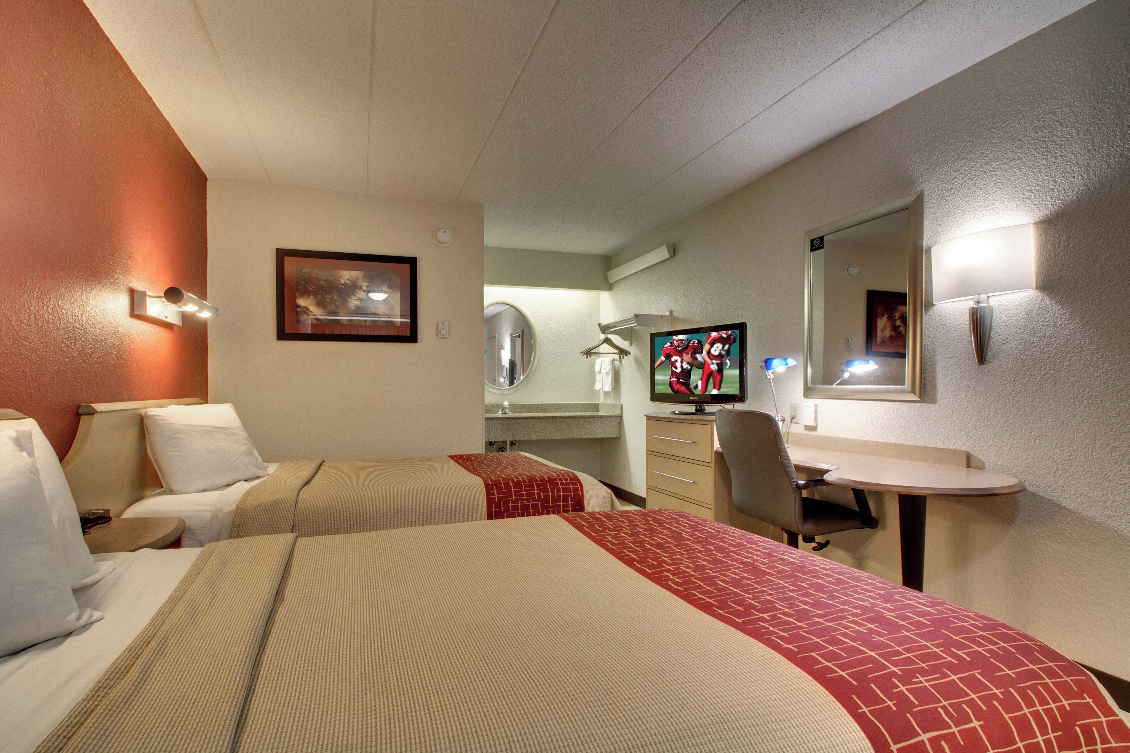 A hotel room with two beds, a desk, a chair, a television, and a mirror.