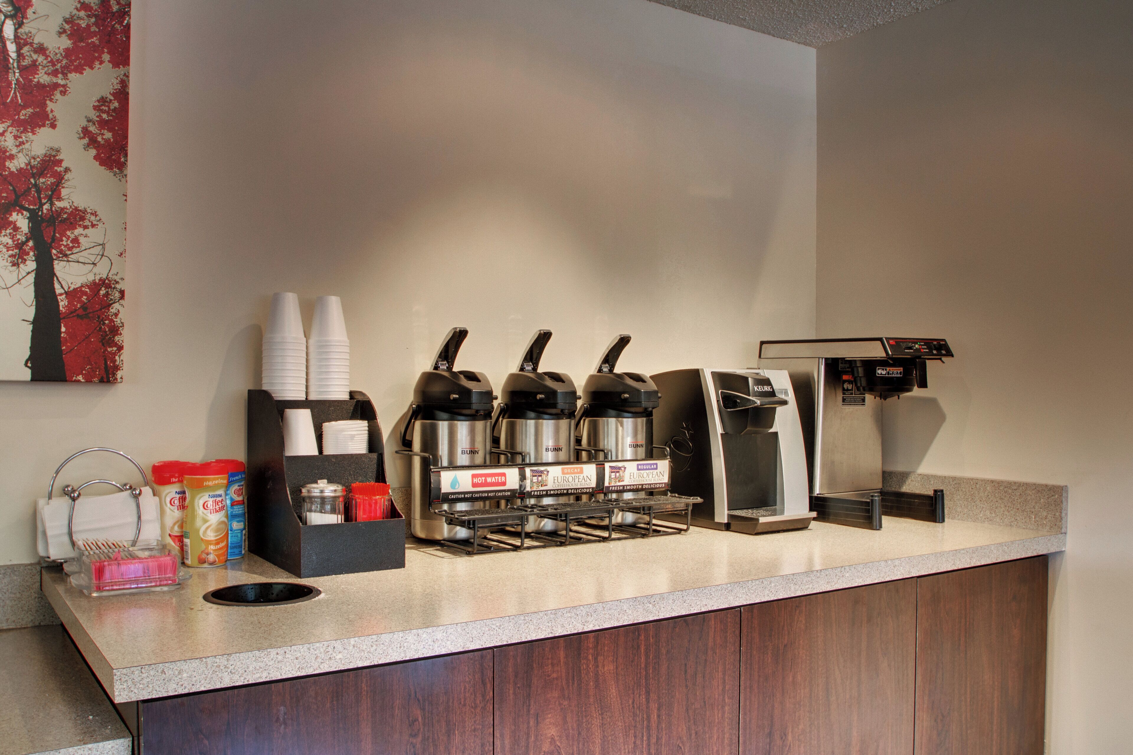 A coffee station with multiple coffee machines, a water dispenser, and a variety of coffee and creamer dispensers.