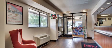 A hotel lobby with a reception desk, a red chair, a large window, and a wall-mounted TV.