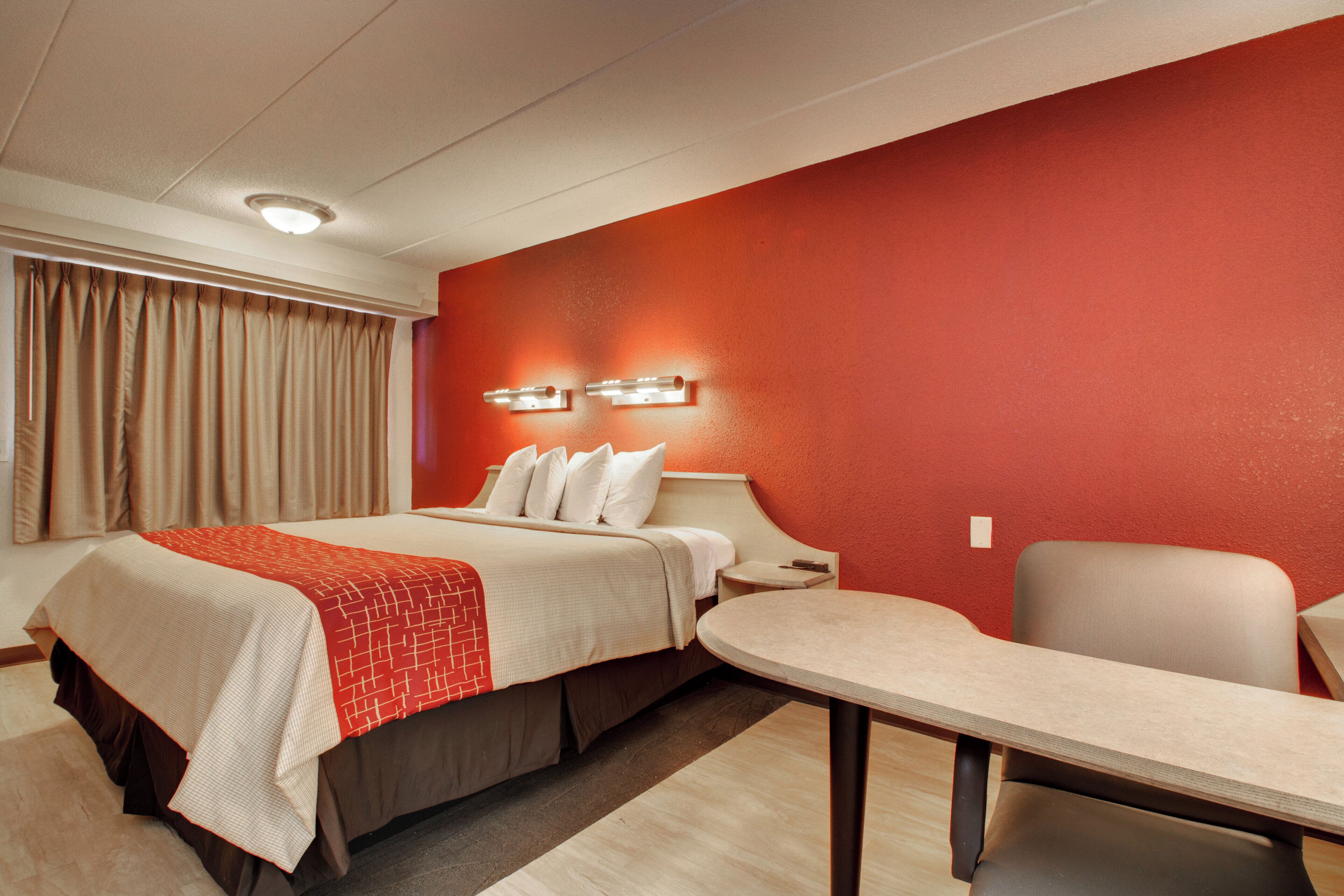 A hotel room with a bed, bedside table, chair, and a red accent wall.