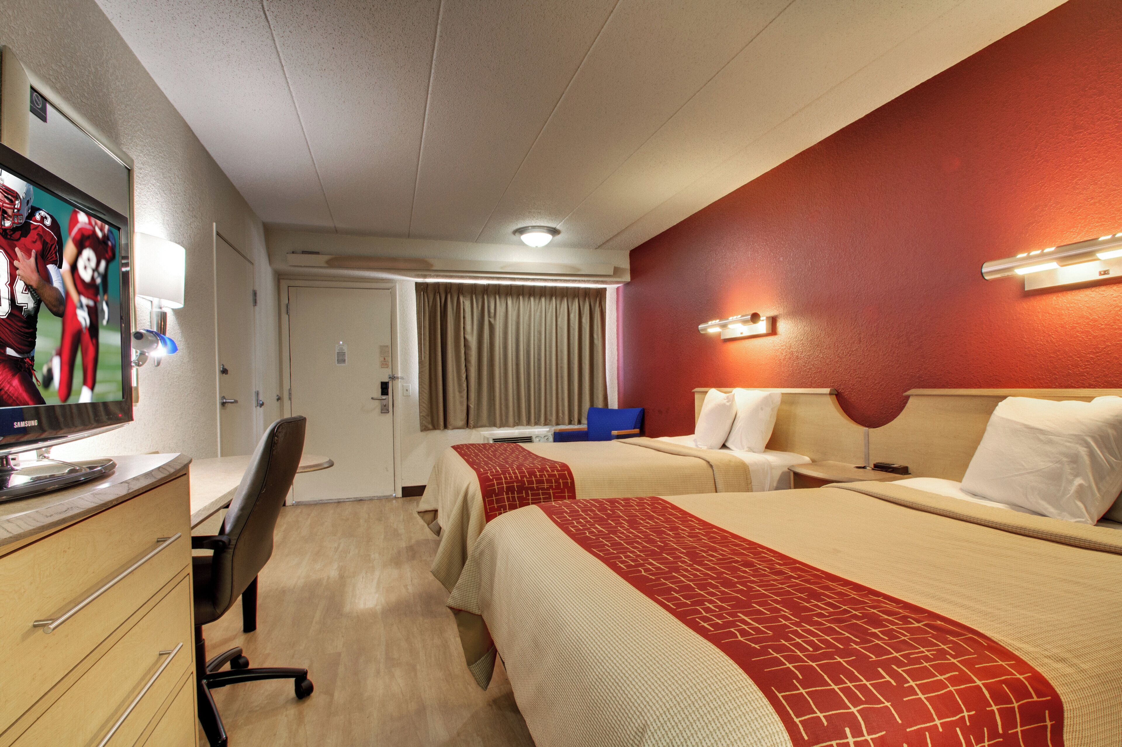 A hotel room with two beds, a desk with a computer, a TV, and a bathroom door.
