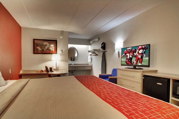 Una habitación de hotel con una cama, un escritorio, una silla, un televisor y un espejo.