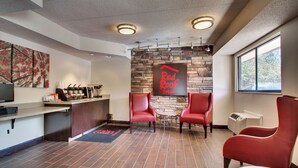 Un interior moderno con pared de piedra, sillas rojas, una estación de café y un letrero de Red Roof Inn.