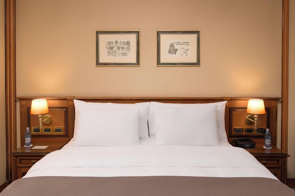 A hotel room with a large bed, two bedside lamps, and two framed pictures on the wall.