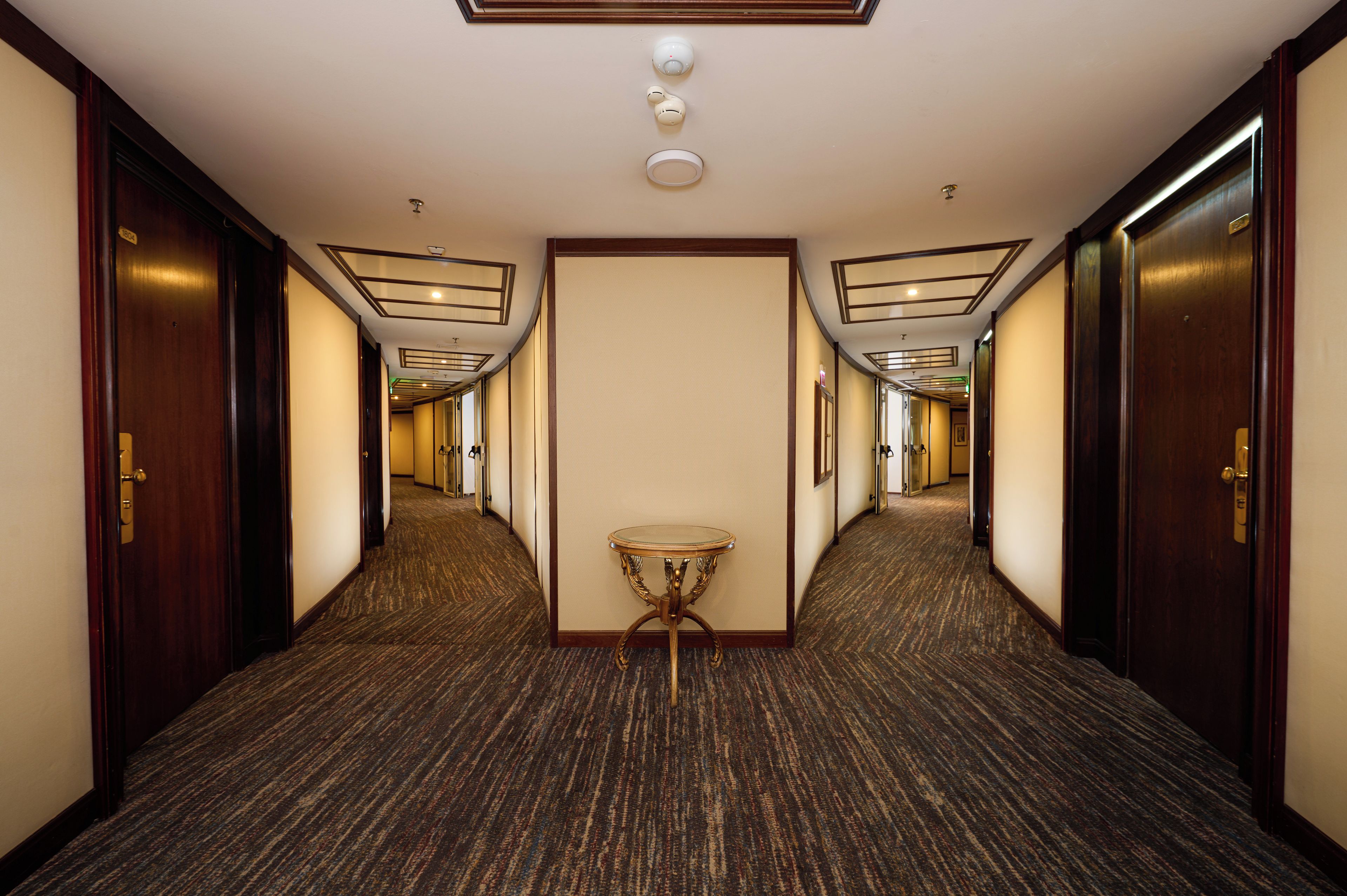 A hotel hallway with carpeted floors, wooden doors, and a small round table in the center.