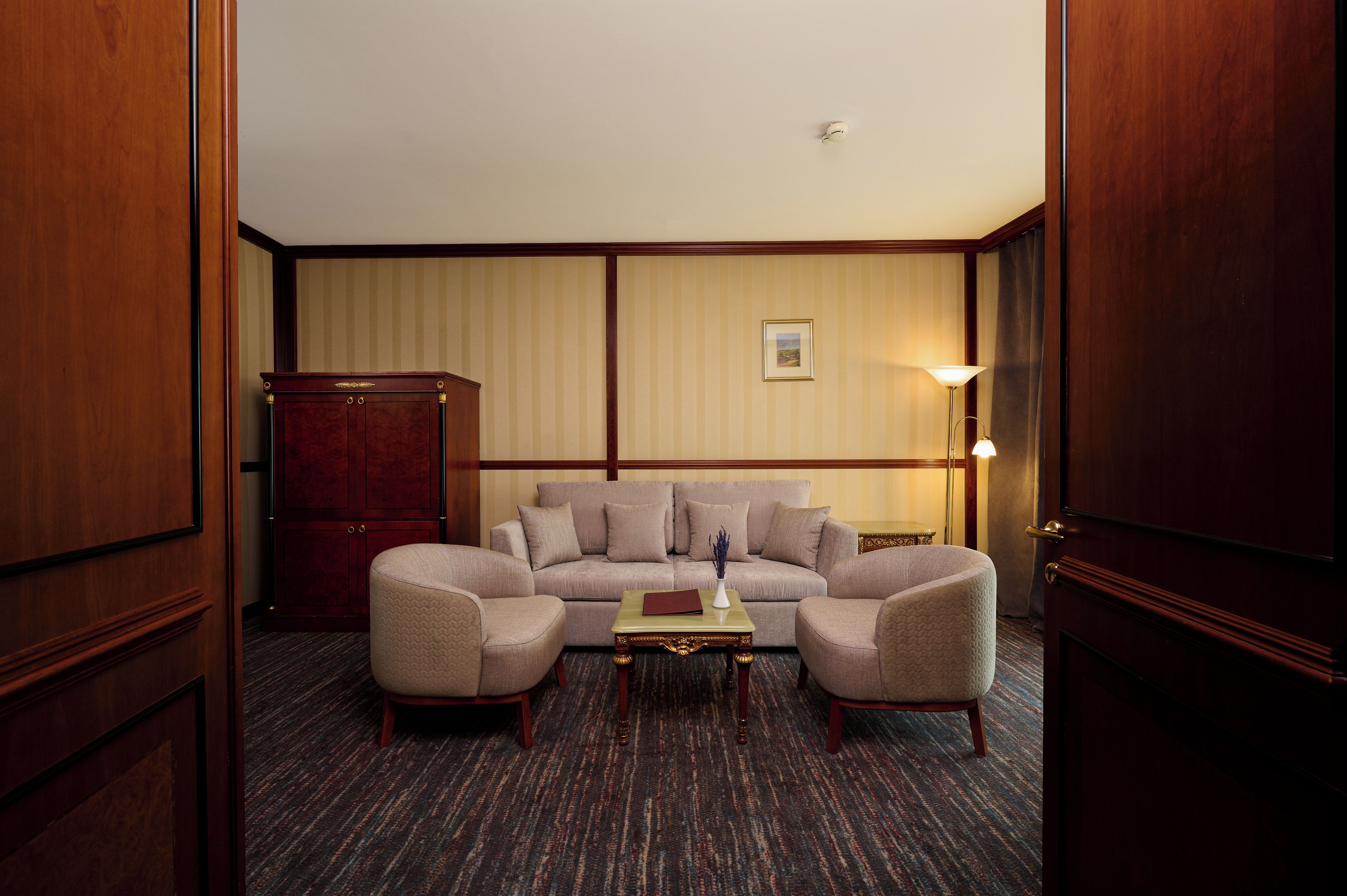 A hotel room with a large sofa set, a wooden cabinet, and a small table with a book.