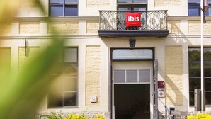 A hotel entrance with a red 'ibis' sign, a brick facade, and a gated entrance. - ibis Douai Centre (Douai)