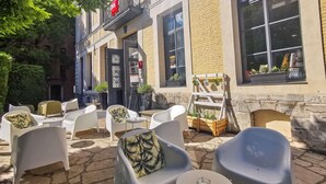 An outdoor seating area with white plastic chairs and tables, a black door with intricate designs, and potted plants on the windowsills. - ibis Douai Centre (Douai)