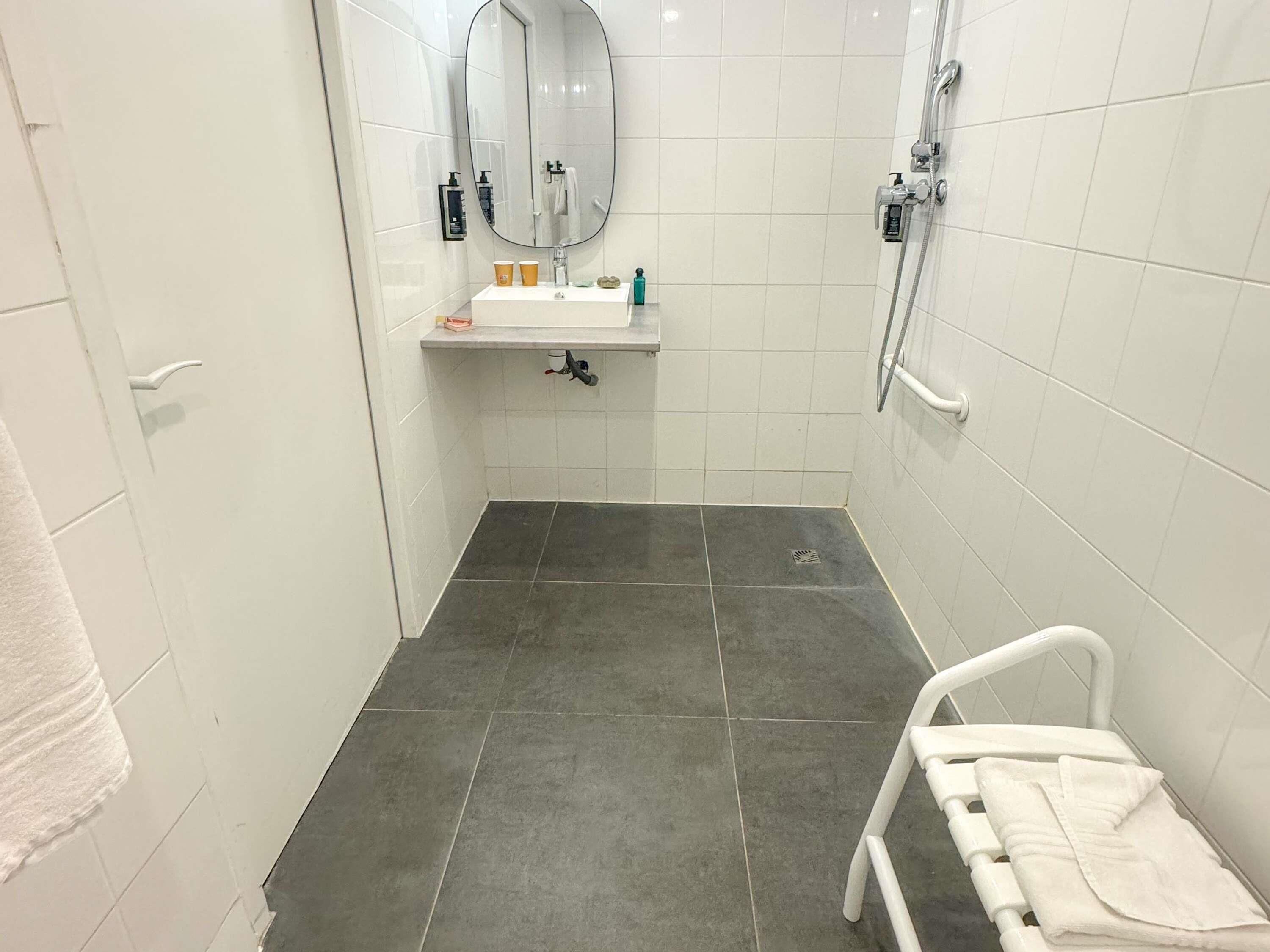 A small, modern bathroom with a white sink, mirror, and shower.