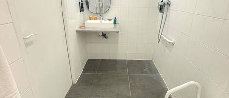 A small, modern bathroom with a white sink, mirror, and shower.