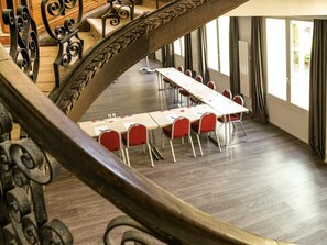 Une salle de conférence avec une longue table, des chaises rouges et un escalier en bois agrémenté de rampes en métal ouvragé.