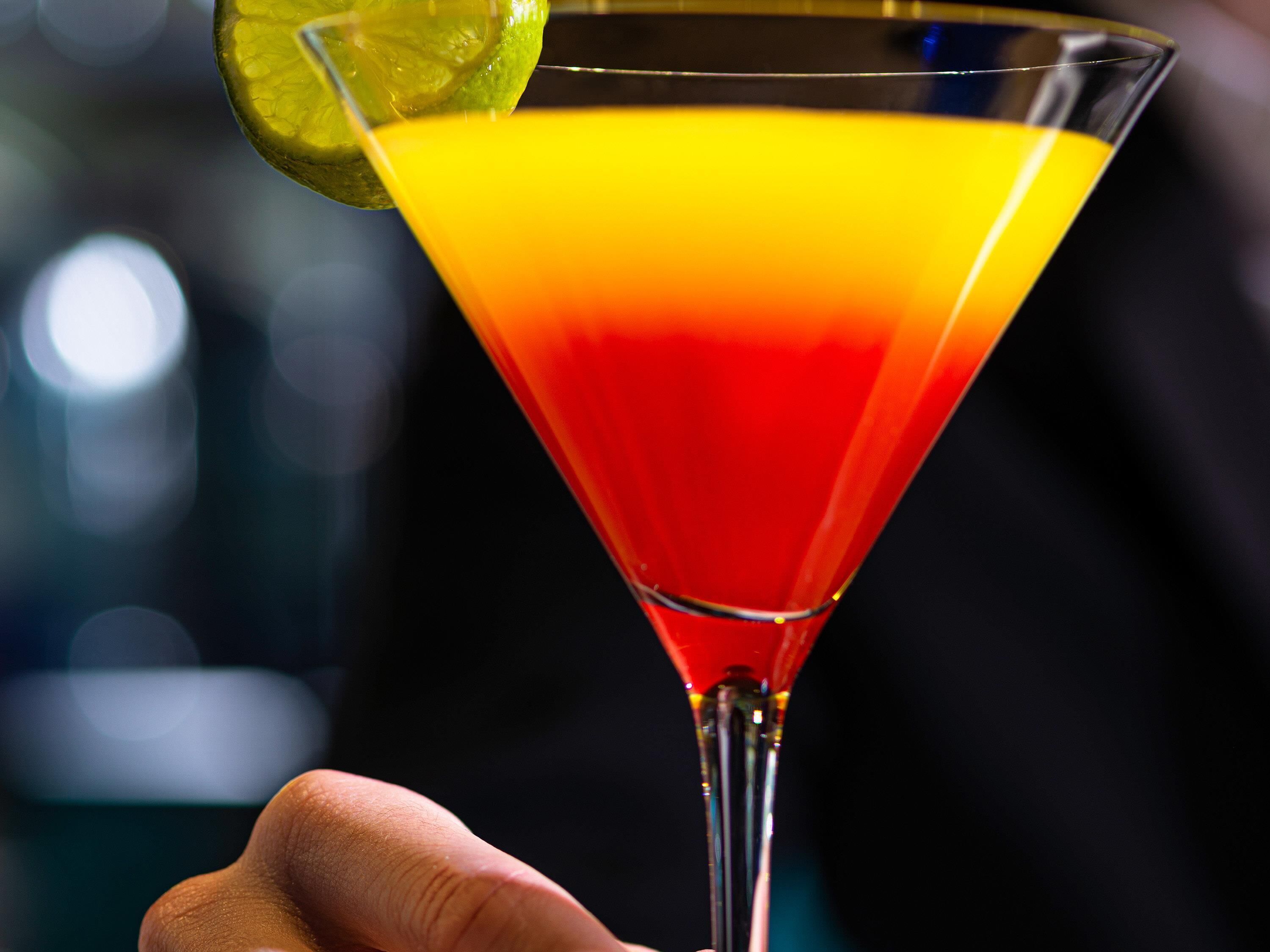 Een cocktailglas met een limoenpartje op de rand, vastgehouden door een hand.