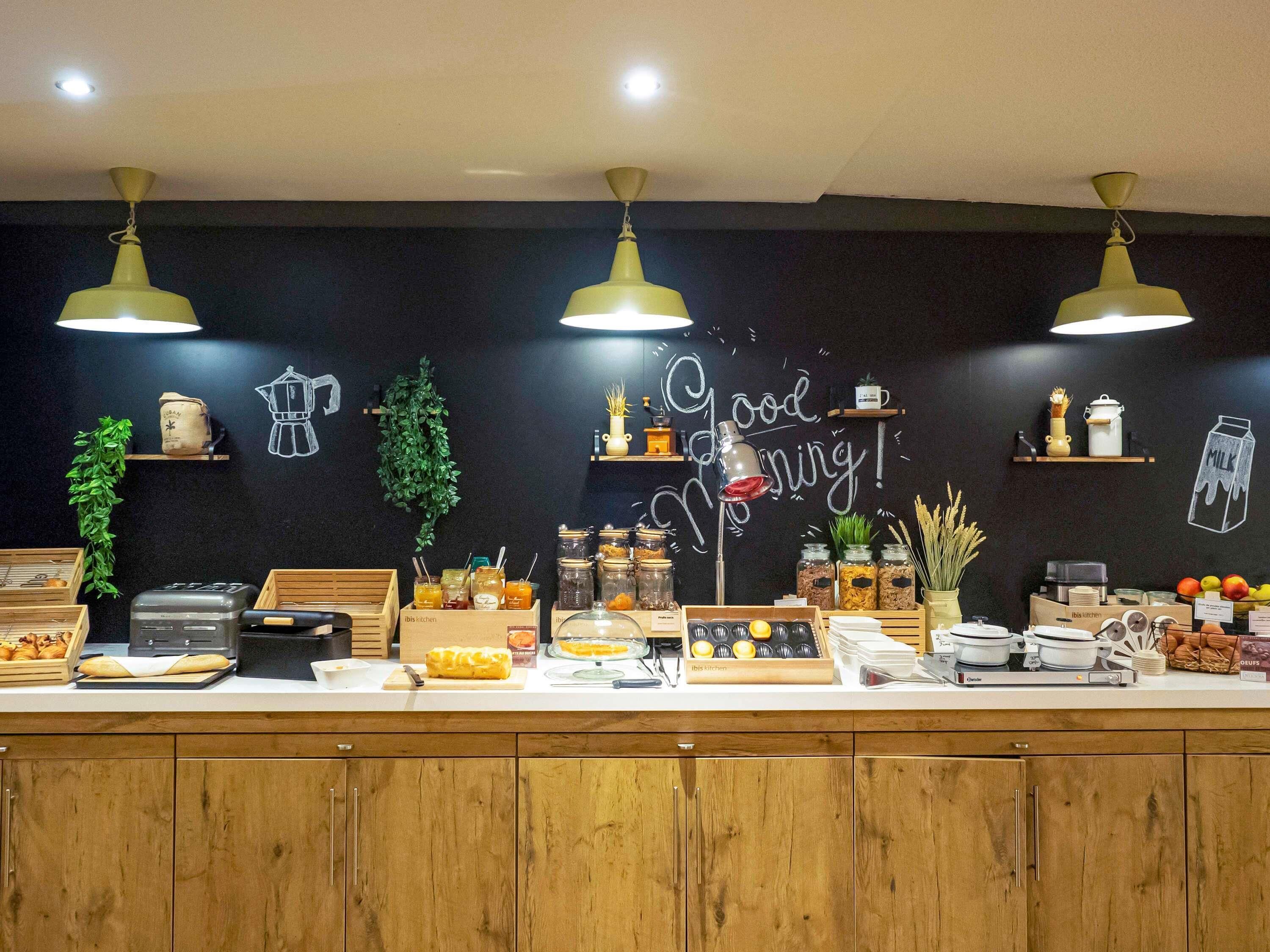 A breakfast bar with a variety of food items and kitchenware, including bread, pastries, and condiments.