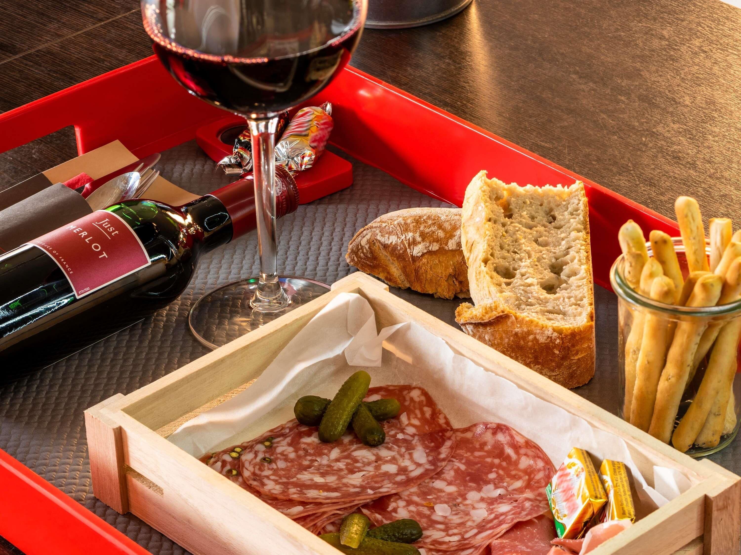 A tray with a bottle of wine, a glass, sliced salami, pickles, bread, and baguettes.