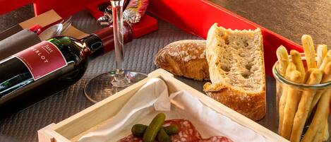 A tray with a bottle of wine, a glass, sliced salami, pickles, bread, and baguettes.