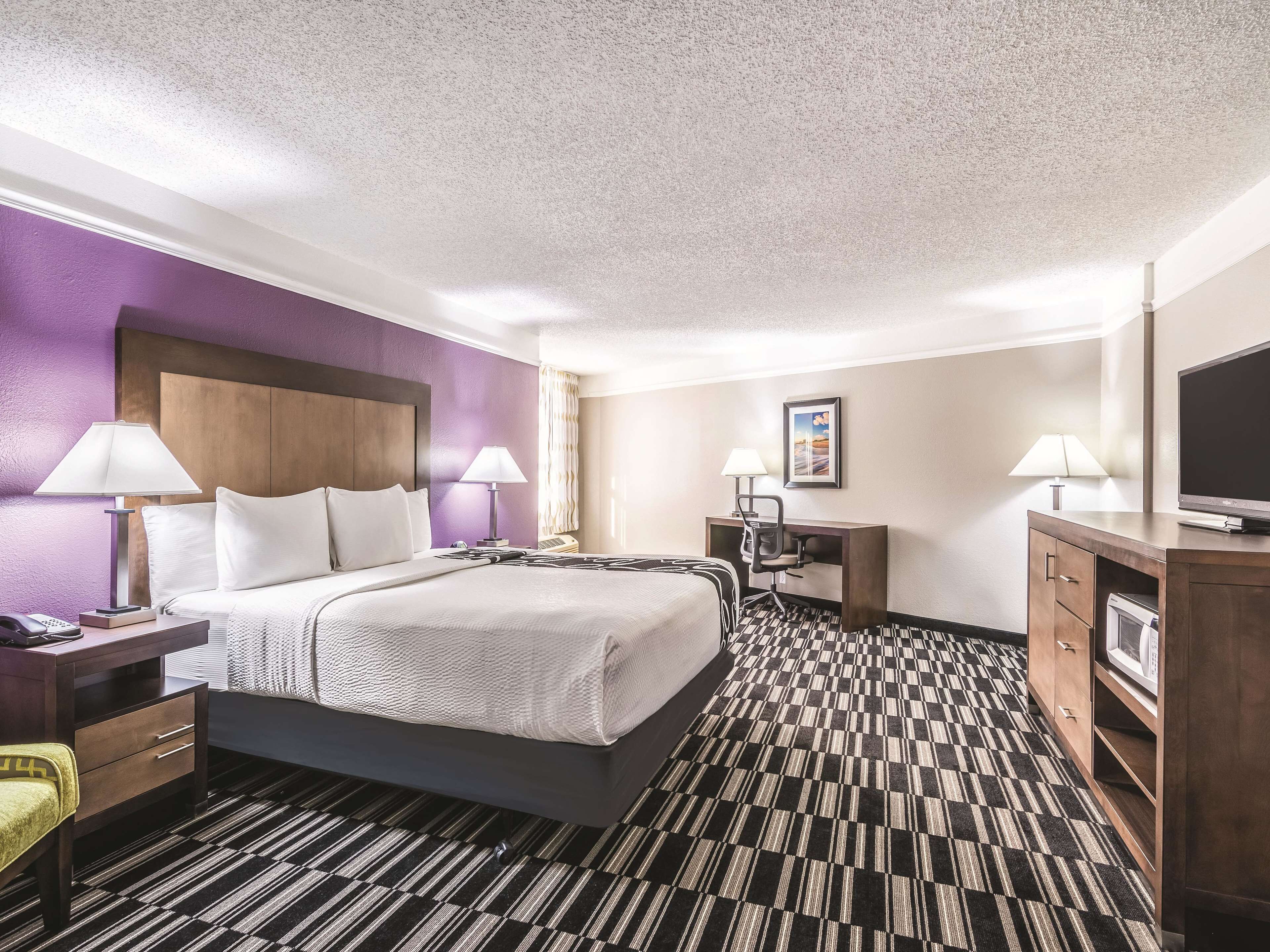 Habitación de hotel con cama, escritorio, silla, televisor y alfombra estampada.